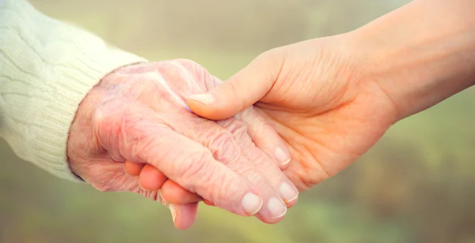 Younger caregiver holding an older adult’s hand to represent stage-by-stage dementia care support